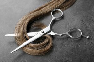 Hairdresser's scissors with strand of brown hair on grey background